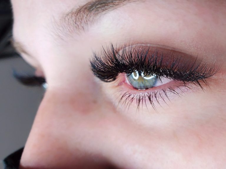 Hybrid Lash Extensions Close-up of a woman's eyes with long lashes and green irises, showing freckles on her skin.